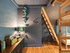 Een kamer met een stapelbed, een bureau met een lamp, een wandlamp en een trap.