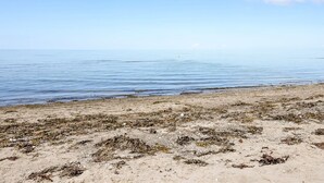 Uma praia com areal dourado e mar calmo sob um céu claro.