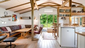 Um espaço de estar acolhedor e integrado, com teto de madeira, área de jantar, cozinha e vista para o verde lá fora.