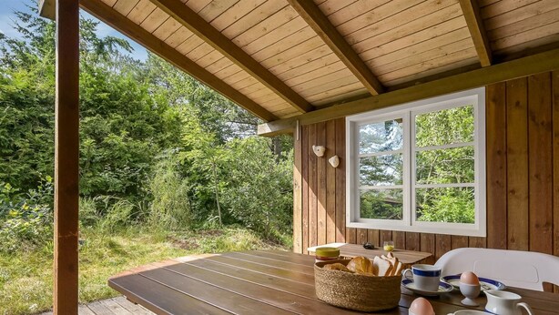 Um deck de madeira com uma mesa posta para o café da manhã, rodeado por vegetação.