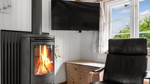 Um quarto aconchegante com lareira a lenha, uma poltrona de couro preto, uma mesa de madeira e uma TV fixada na parede.