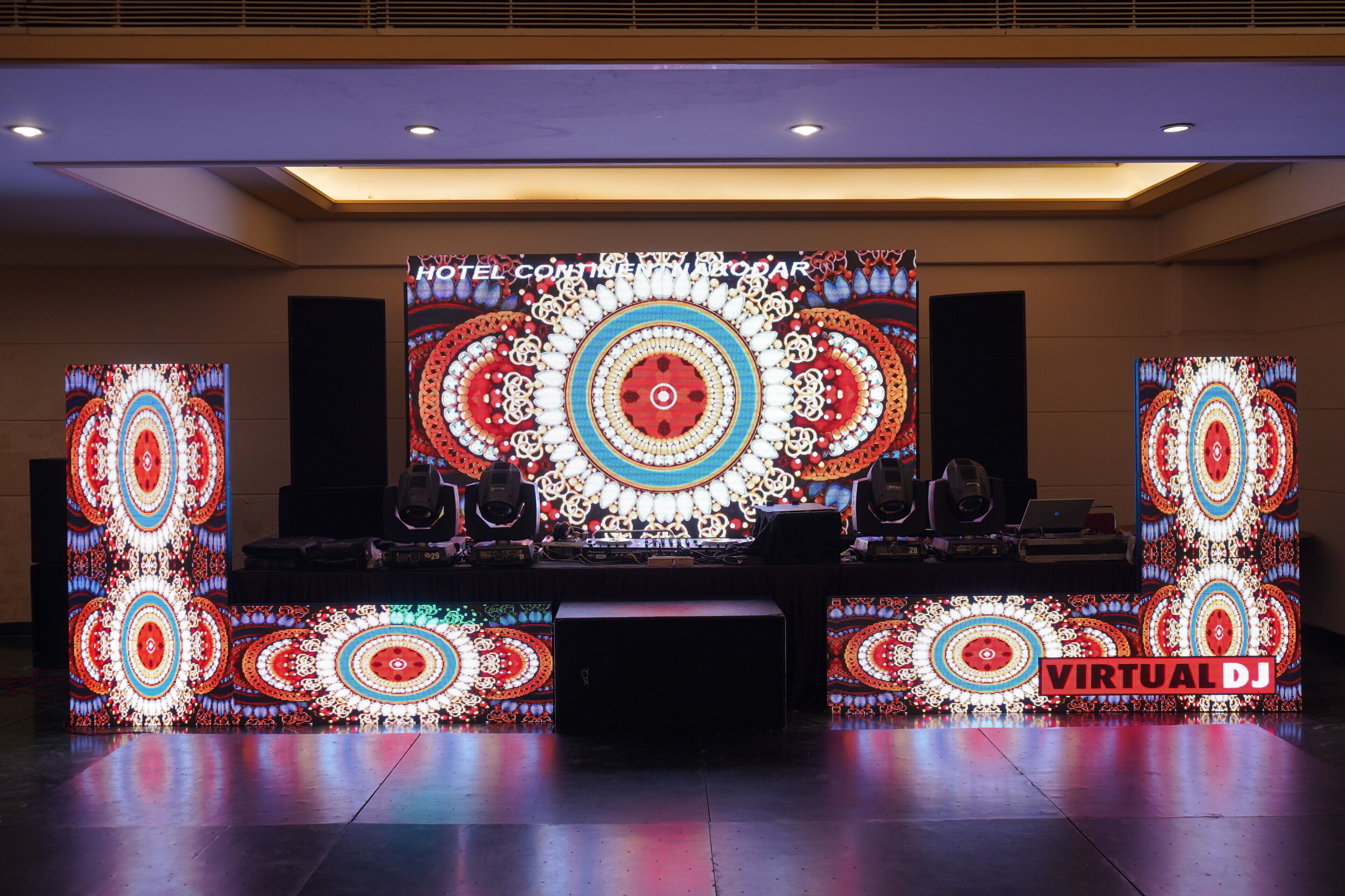 A hotel reception area with a large digital display, a desk with audio equipment, and a sign reading "VIRTUAL DJ".