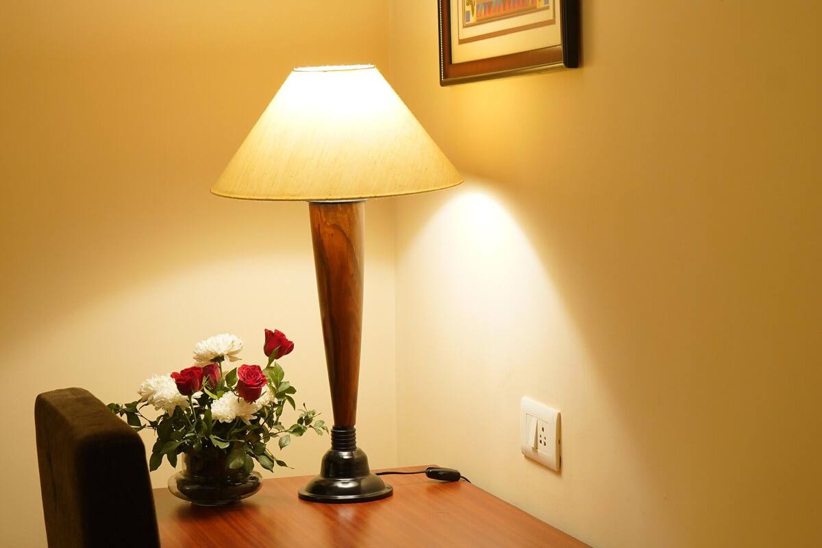 A wooden table with a lamp, a vase of flowers, and a framed picture on the wall.