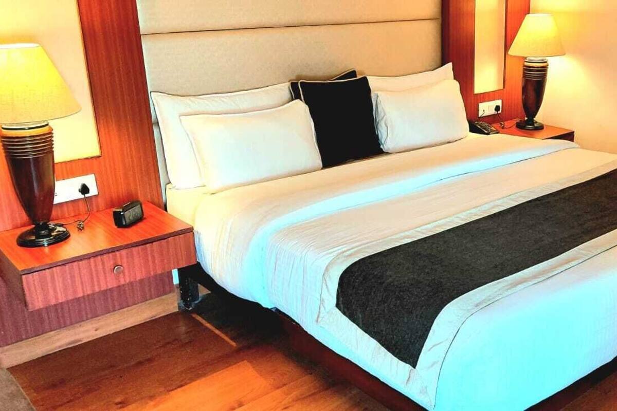 A neatly made bed with white and black bedding, two bedside lamps, and a wooden nightstand with a phone and a power outlet.