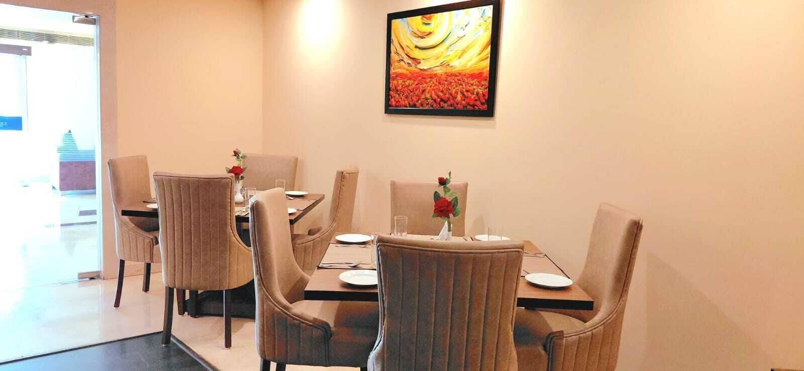Uma sala de jantar com seis cadeiras e uma mesa, cada uma com um prato e um copo. Um vaso com flores vermelhas está sobre a mesa.