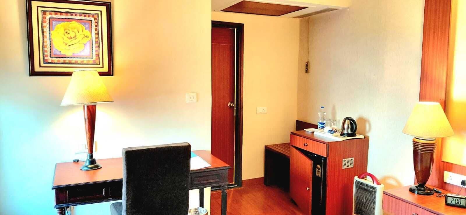 A hotel room with a desk, two lamps, a chair, a small cabinet, and a door.