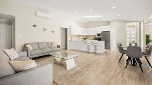 Una sala de estar moderna con un sofá gris, una mesa de centro de vidrio y un comedor con una mesa y sillas de vidrio.