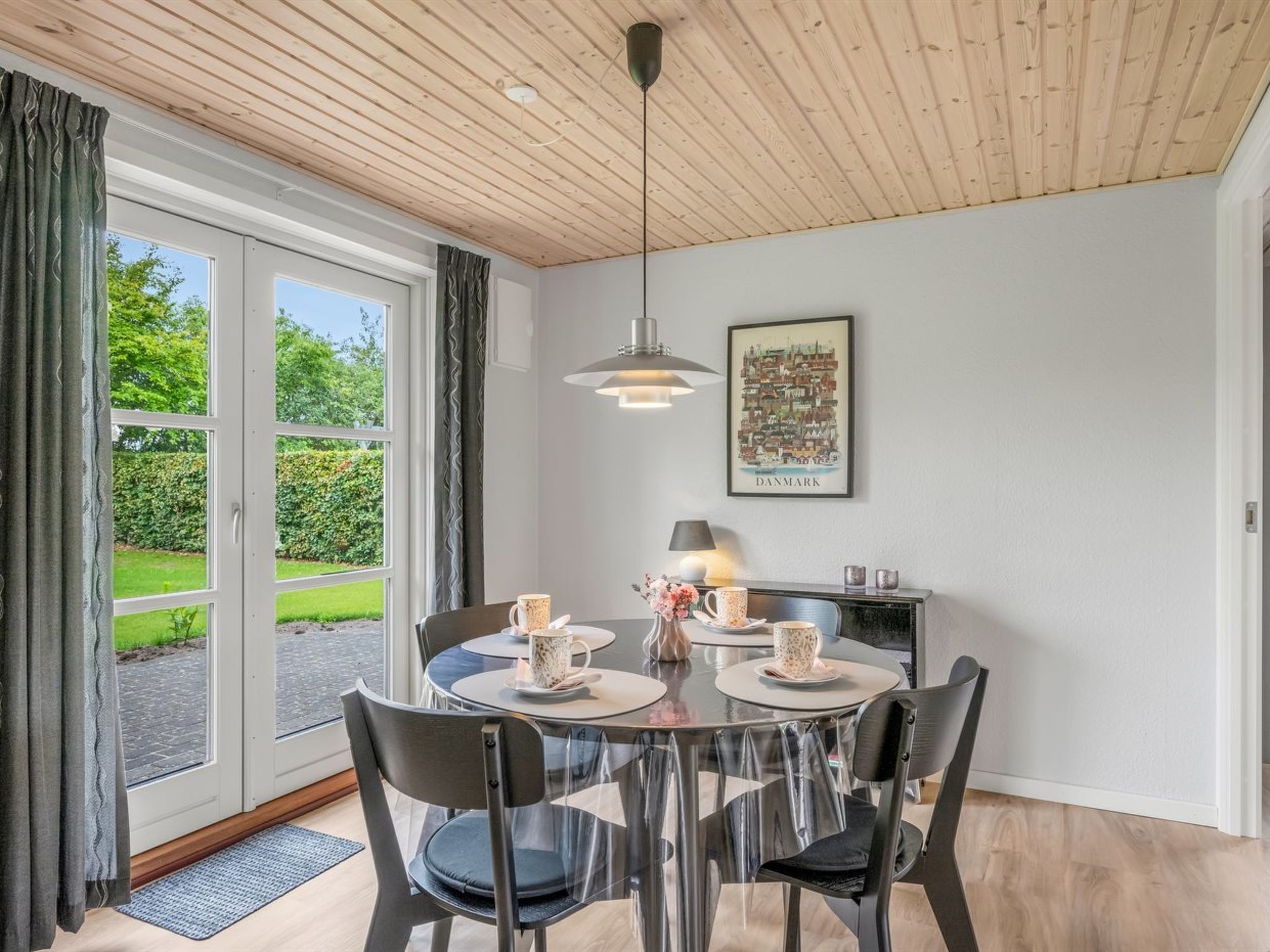 Ein Essbereich mit einem runden Tisch, Stühlen und Blick auf einen Garten durch große Fenster.