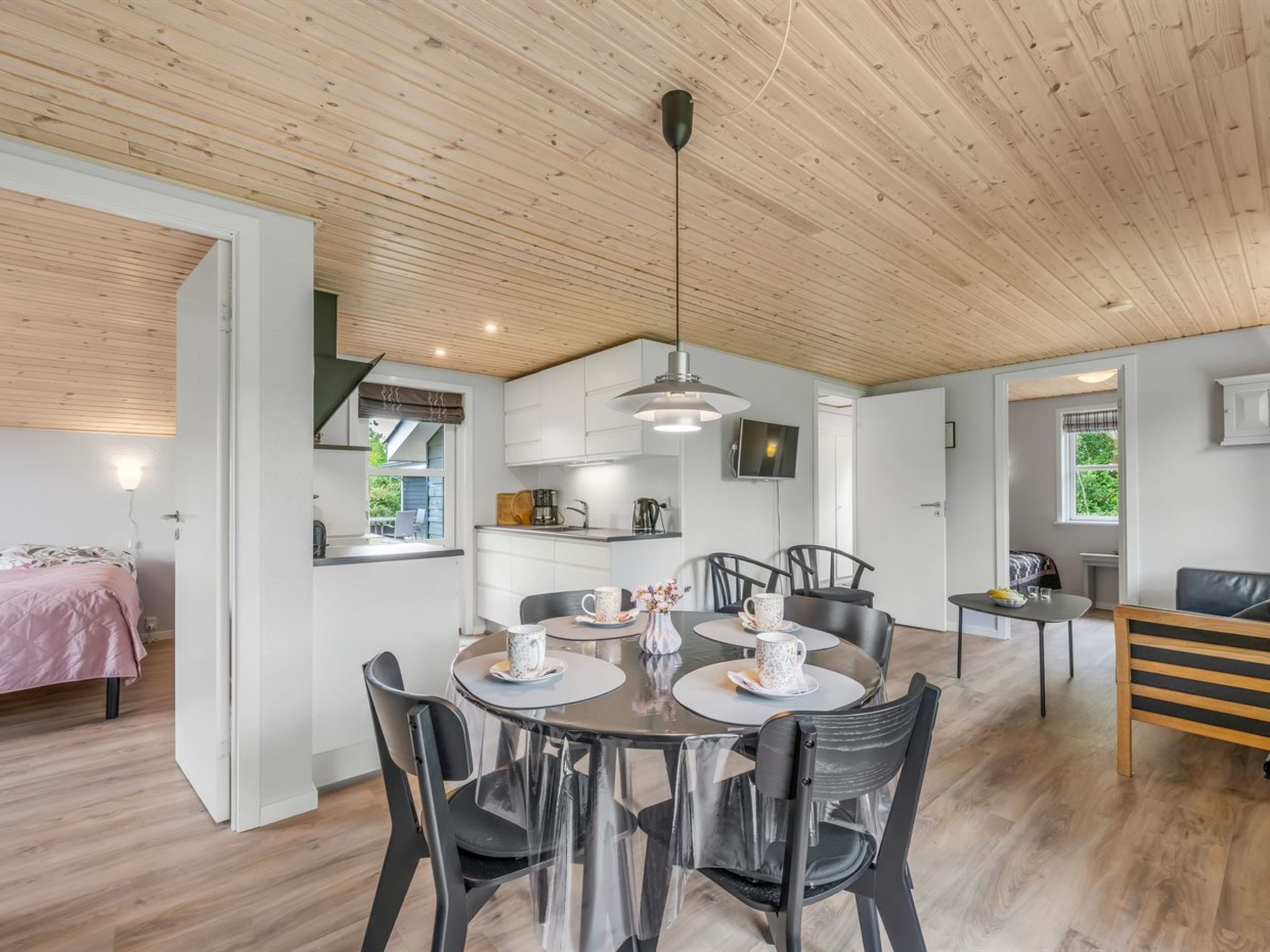 Een moderne keuken met witte kasten, een eethoek met een ronde tafel en stoelen, en een houten plafond.