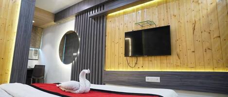 A modern hotel room with a large bed, a flat-screen TV mounted on the wall, and a wooden panel design.