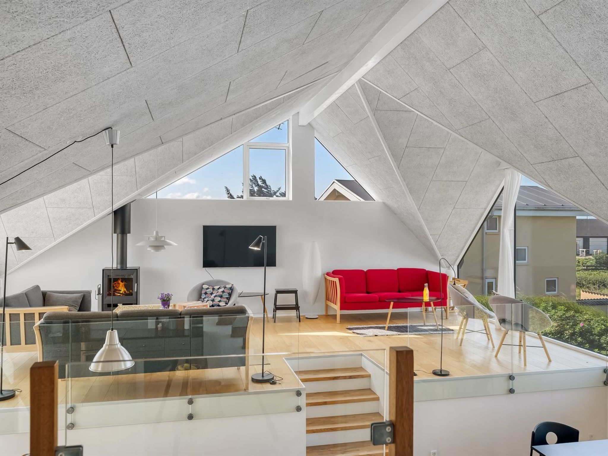 Un loft moderne avec un plafond haut, une cheminée, un canapé rouge et un téléviseur fixé au mur.