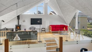 Un loft moderno con techo alto, chimenea, sofá rojo y televisor montado en la pared.