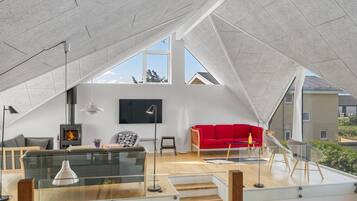 Un loft moderne avec un plafond haut, une cheminée, un canapé rouge et un téléviseur fixé au mur.