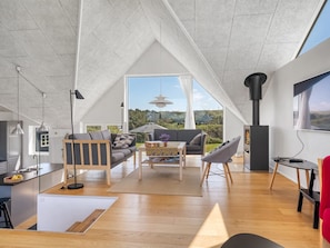 Un loft spacieux avec un plafond haut, un coin cuisine, un espace salon avec un canapé et des fauteuils, et une grande fenêtre offrant une vue sur l’extérieur.