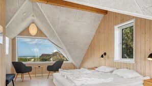 Un dormitorio con una cama grande, dos sillas, una mesita pequeña, una ventana con vistas y un techo inclinado.