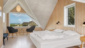 Une chambre à coucher avec un grand lit, deux chaises, une petite table, une fenêtre donnant sur un beau paysage et un plafond en pente.