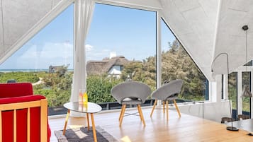 Un intérieur moderne avec une grande fenêtre, un canapé rouge, deux fauteuils gris et une petite table ronde.
