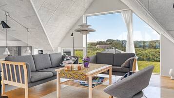 Ein modernes Schlafzimmer im Loft-Stil mit schrägem Dach, großem Fenster und Blick ins Grüne.