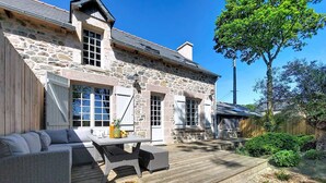 A stone house with a deck, wicker furniture, and a wooden fence.