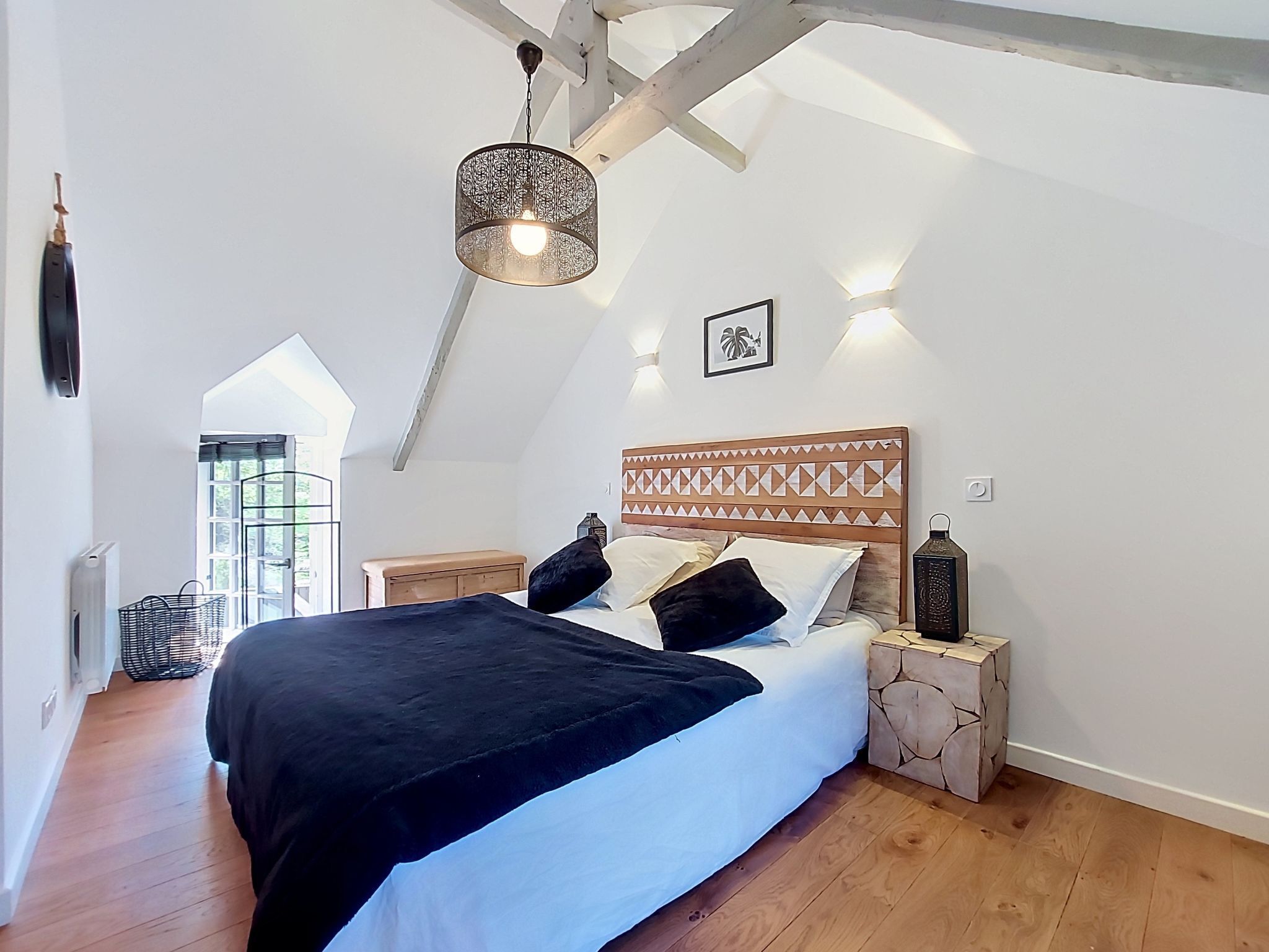 Une chambre avec un plafond haut, un lit doté d’une tête de lit à motifs, des lampes de chevet et une fenêtre offrant une vue agréable.