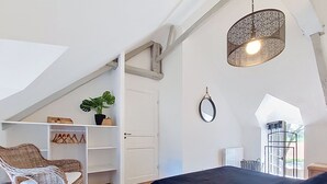 A bedroom with a bed, a chair, a hanging light fixture, a door, and a window.
