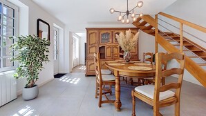 A dining area with a wooden table, chairs, a chandelier, and a staircase.
