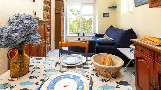A cozy living room with a dining area, featuring a table set for two, a blue sofa, and a window with a view of greenery. - Theophile by Interhome (Saint Malo)