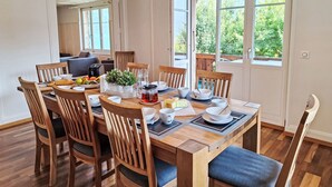 Uma área de refeições com uma mesa de madeira posta para quatro pessoas, cercada por cadeiras de madeira com almofadas azuis.