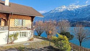 A wooden house with a tiled roof overlooking a lake and snow-capped mountains.