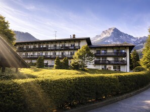 Un hotel de varios pisos con balcones, rodeado de vegetación exuberante y montañas al fondo.