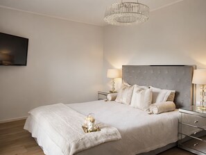 Un dormitorio moderno con una cama grande, dos mesitas de noche, una araña y un televisor de pantalla plana montado en la pared.
