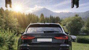 Un coche negro estacionado en una carretera, con una montaña y árboles al fondo.