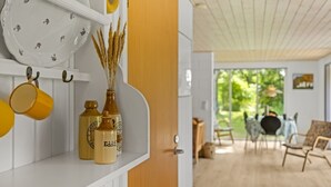 Ein modernes Interieur mit einem weißen Regal, das dekorative Gegenstände beherbergt, und einer gelben Tür, die in einen Essbereich mit Tageslicht führt.