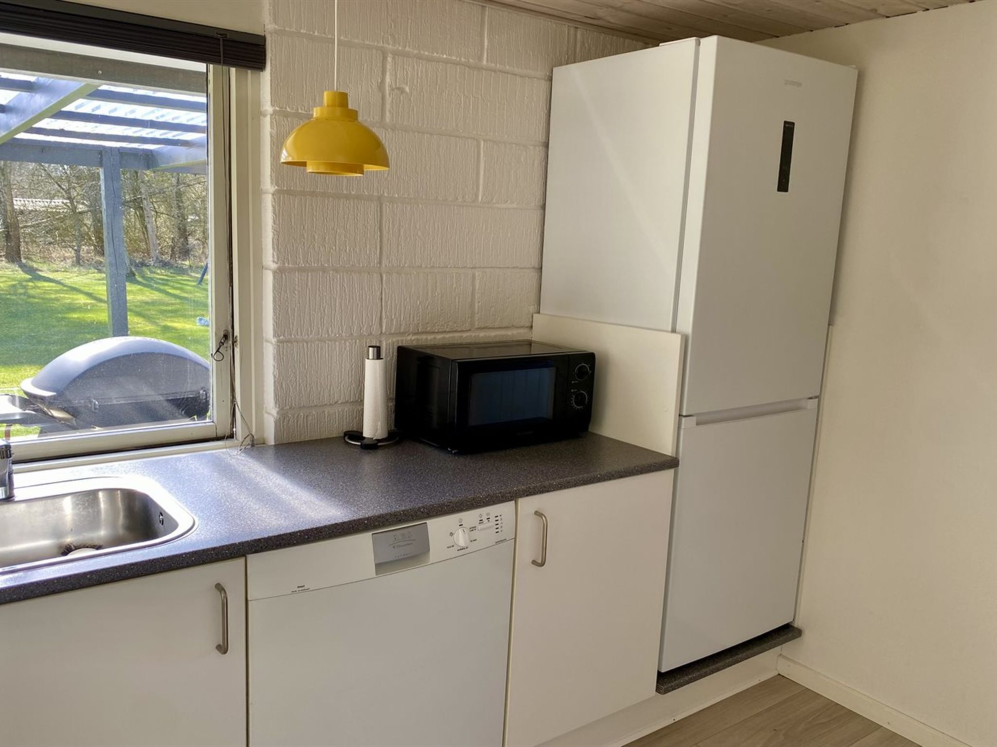 A compact kitchen with a microwave, a refrigerator, a sink, and a yellow pendant light.