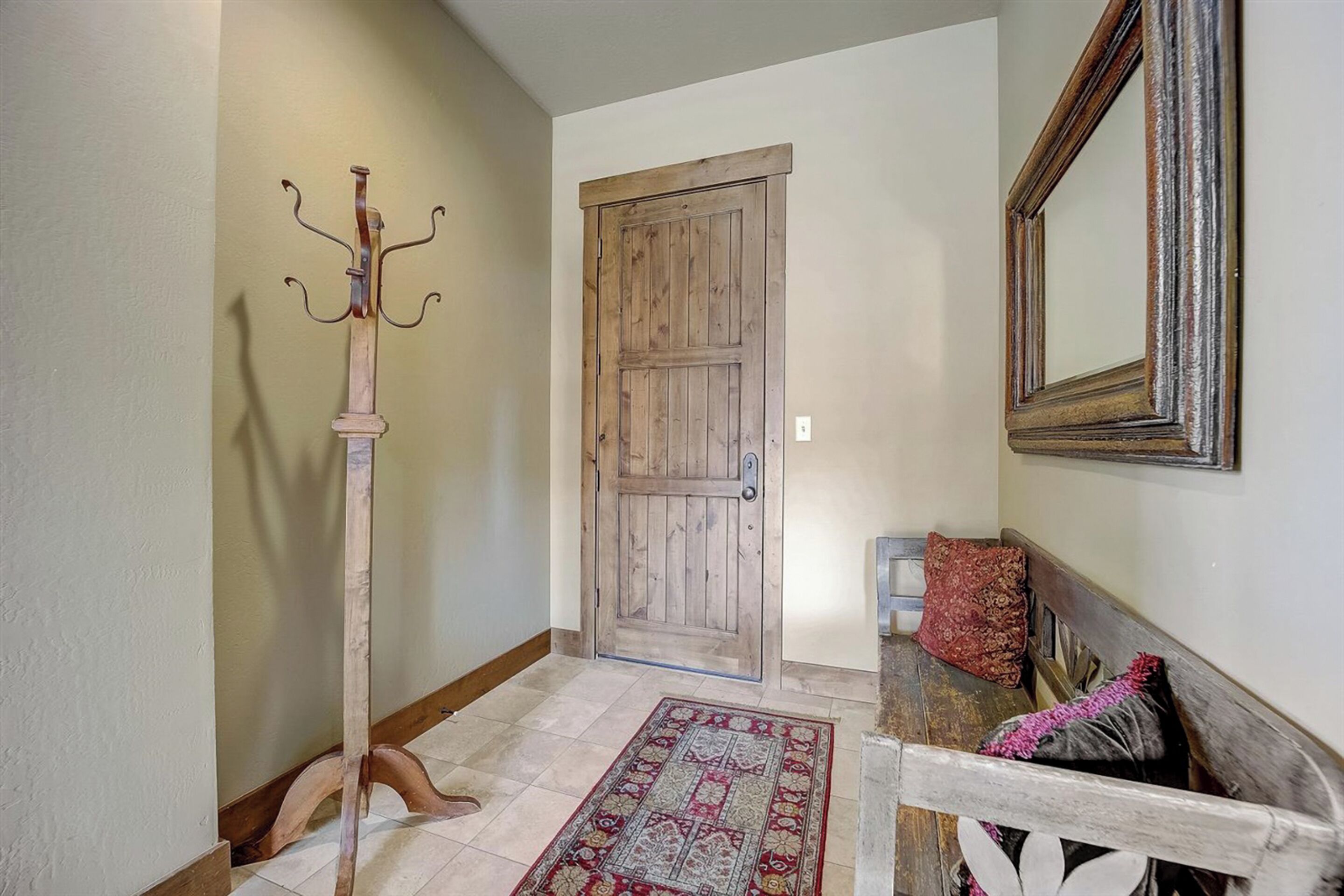 Un corridoio con una porta in legno, un appendiabiti, una panca con cuscini e un tappeto decorato.