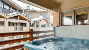 A hot tub on a balcony with wooden railings, overlooking a residential area with multiple buildings.