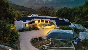 Une maison moderne dotée d’un toit incurvé, entourée d’un jardin et offrant une vue sur un paysage montagneux.