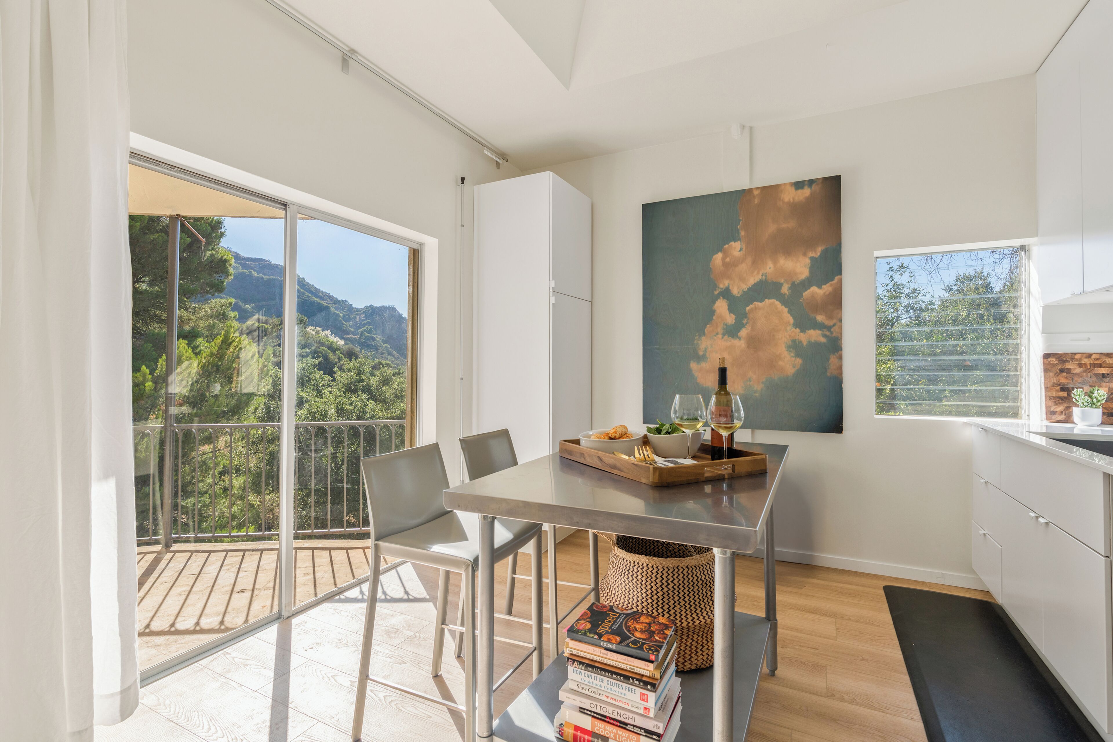 A modern kitchen with a dining area, large windows, and a view of the outdoors.