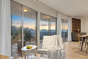 Ein modernes Wohnzimmer mit einem großen Schiebeglasfenster, das auf einen Balkon mit Bergblick führt.