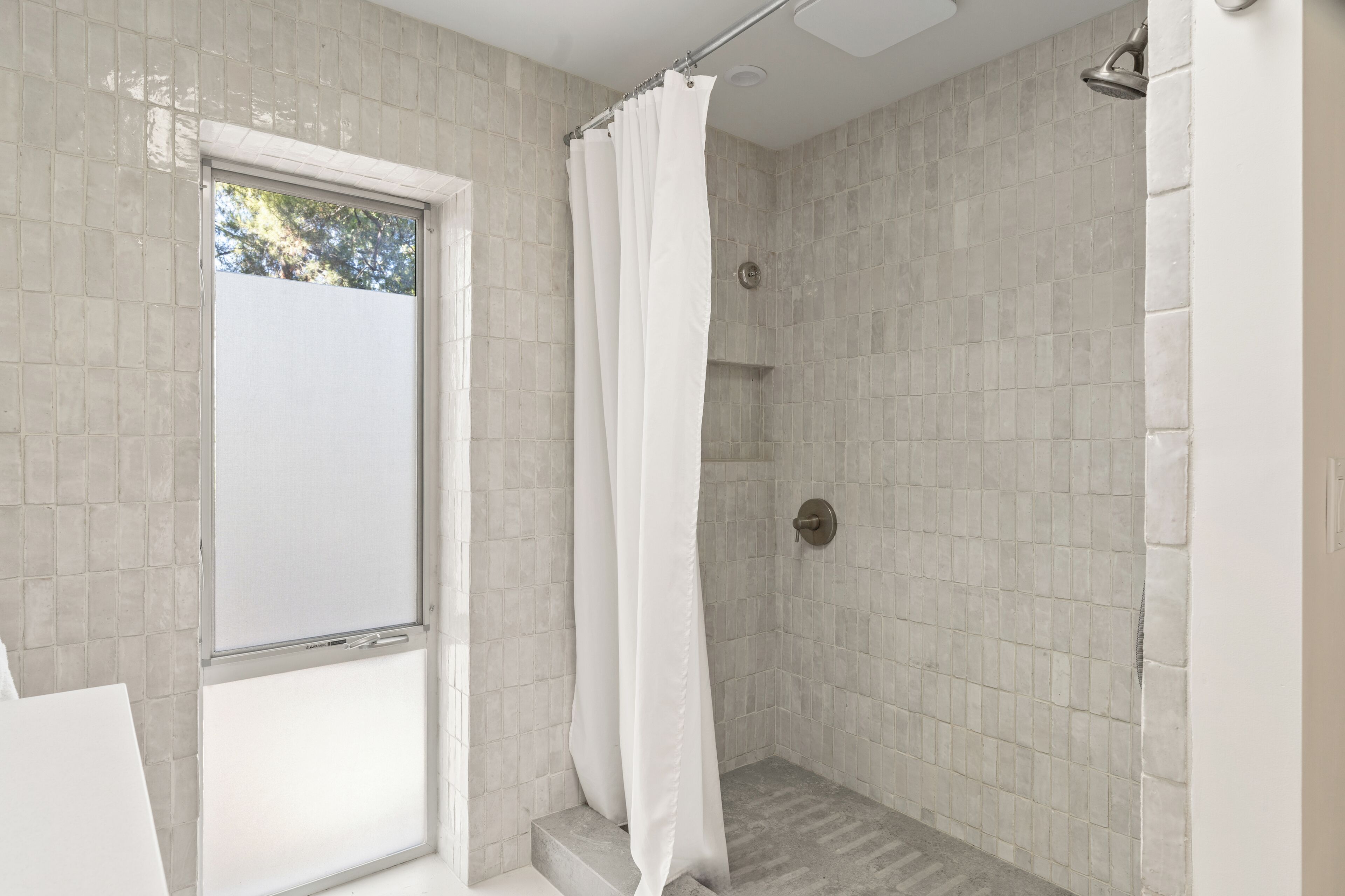 Ein modernes Badezimmer mit Duschbereich, gefliesten Wänden und einem Fenster.