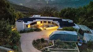 Una casa moderna con techo curvo, rodeada de un jardín y con vistas a un paisaje montañoso.
