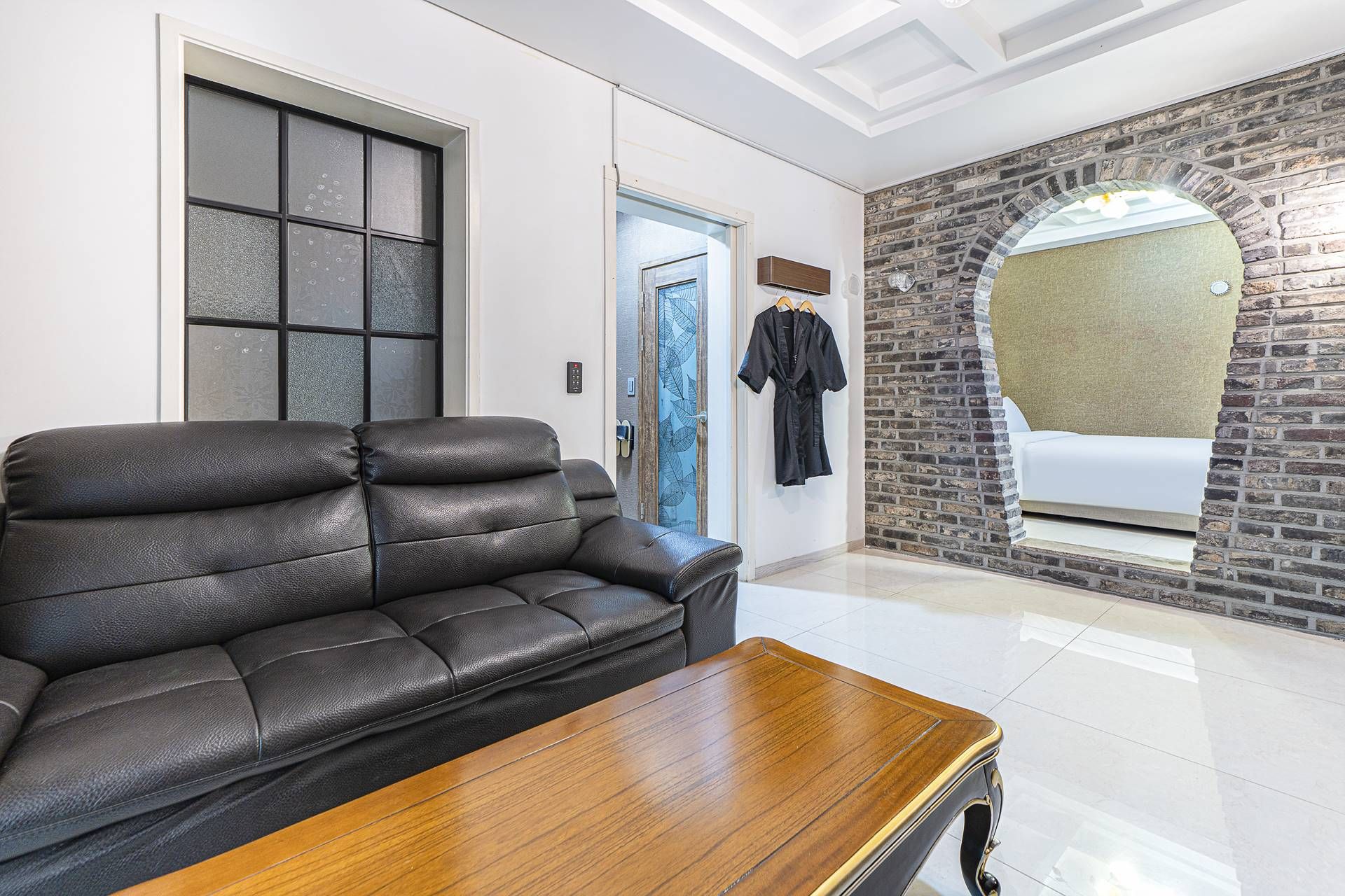 A modern living room with a leather sofa, a wooden coffee table, a stone accent wall, and a glass door leading to another room.