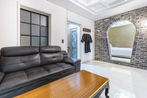 Una sala de estar moderna con un sofá de cuero, una mesa de centro de madera, una pared de acento de piedra y un ventanal que da a otra habitación.