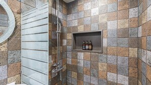 A bathroom with a shower, a glass door, and a shelf with toiletries.