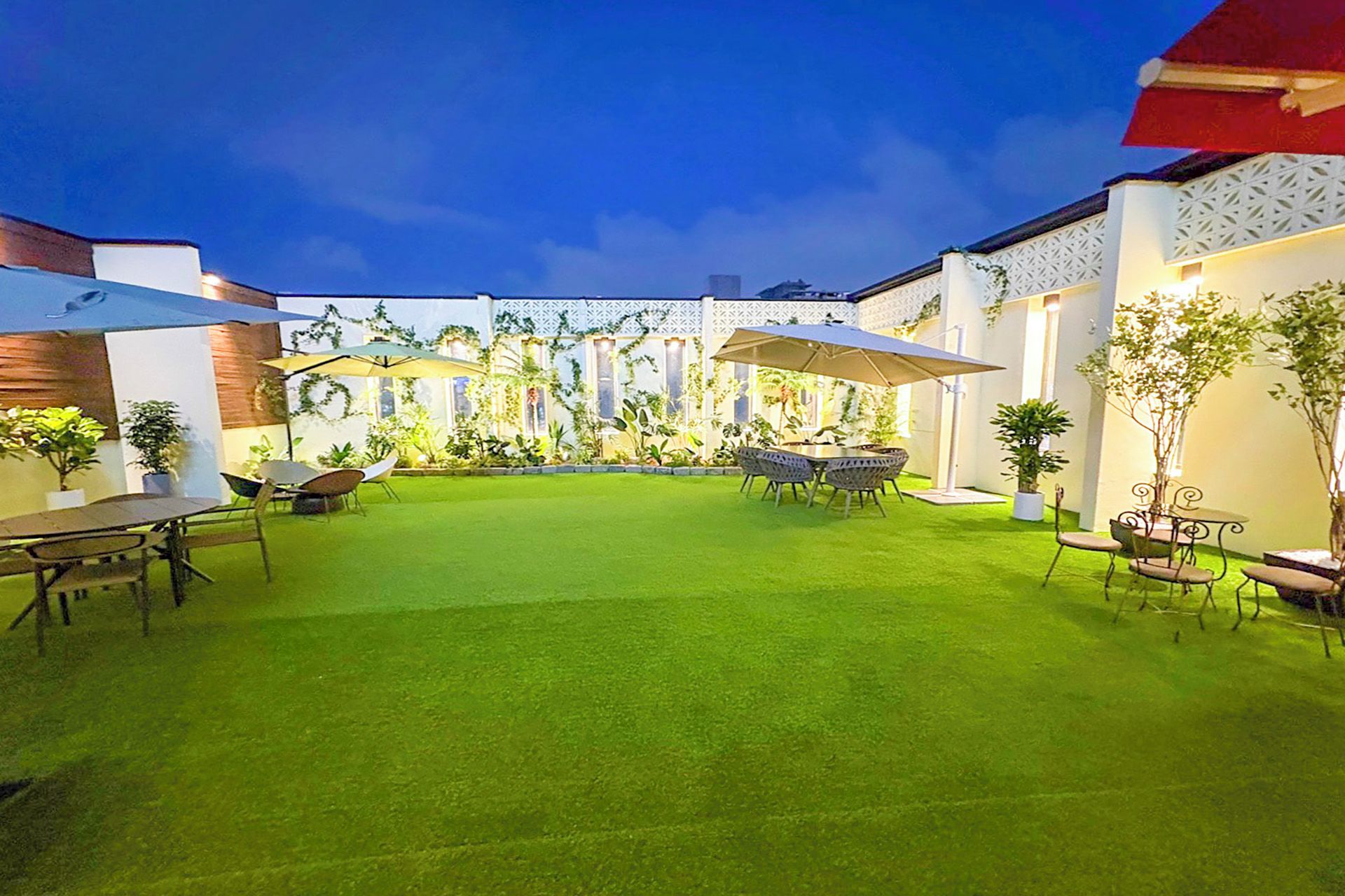Un patio al aire libre bien cuidado, con césped, mesas, sillas y sombrillas.