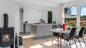 A modern kitchen with a central island, a dining area with a round table and chairs, and a large window providing a view of the outdoors. - "Sinikka" - 900m from the sea by Interhome (Blåvand)