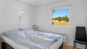 A bedroom with a bed, a chair, a bedside table, a window with a view of trees, and a ceiling light. - "Sinikka" - 900m from the sea by Interhome (Blåvand)