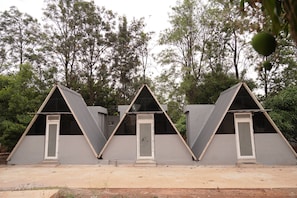 Three triangular tents with doors, set against a backdrop of trees. - Benchkal Resort (Tumkur)