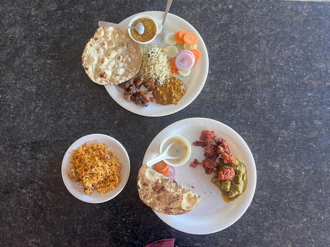Una mesa con tres platos de comida, incluyendo pan plano, arroz y varios curries.