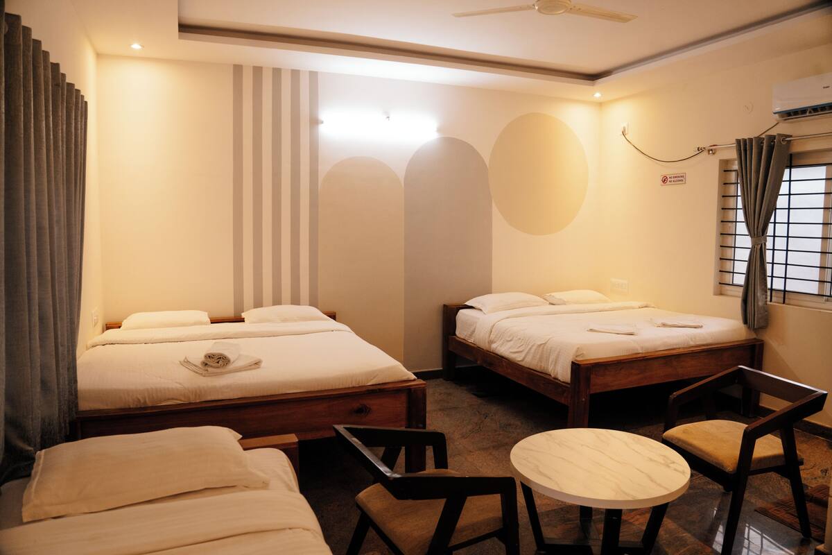 A hotel room with two beds, a small round table, a chair, and a ceiling fan.